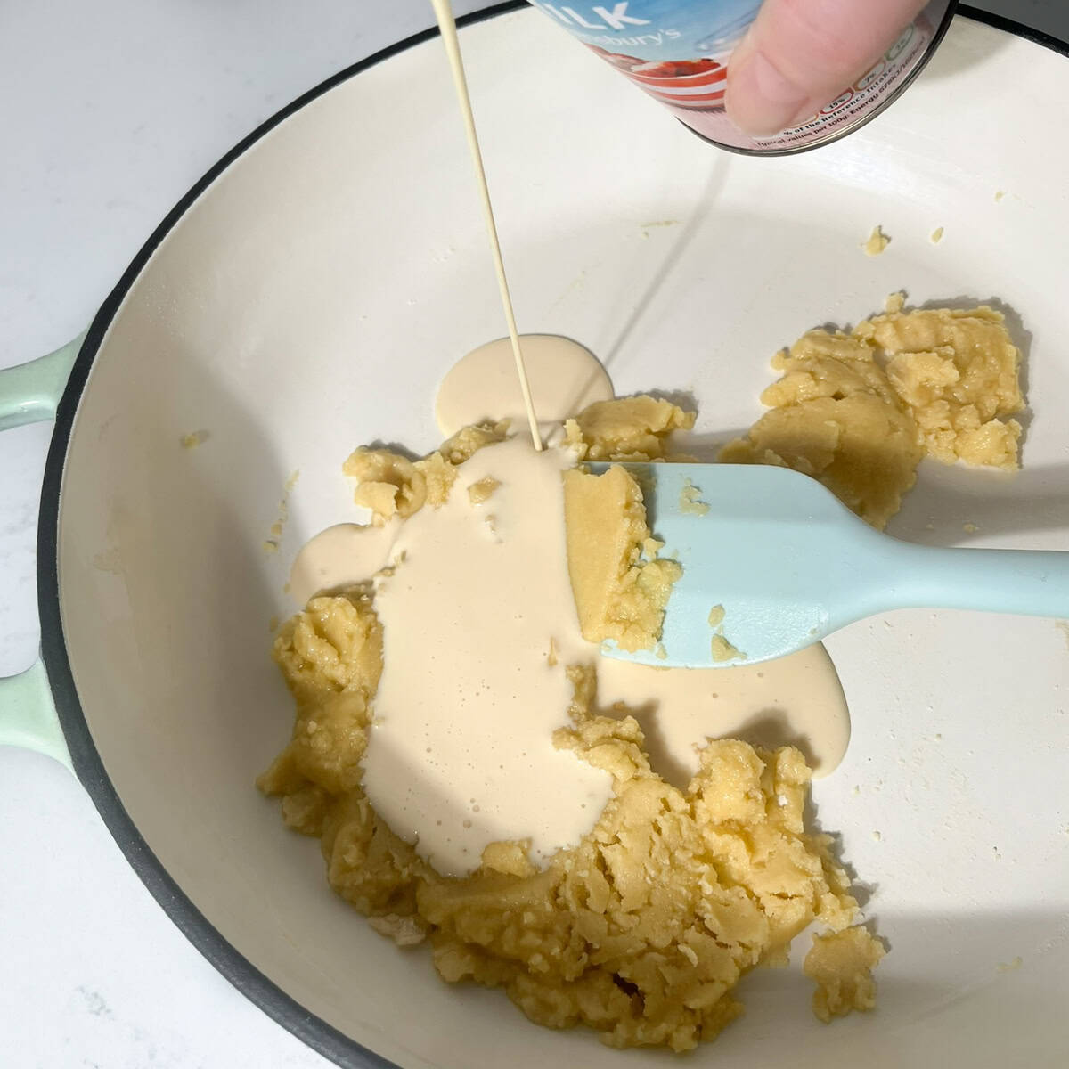 Adding evaporated milk to the roux in a large saucepan.