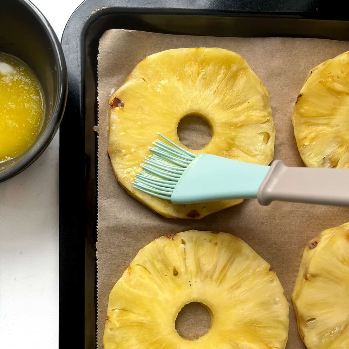 Brushing pineapple rings on a baking tray with melted butter.