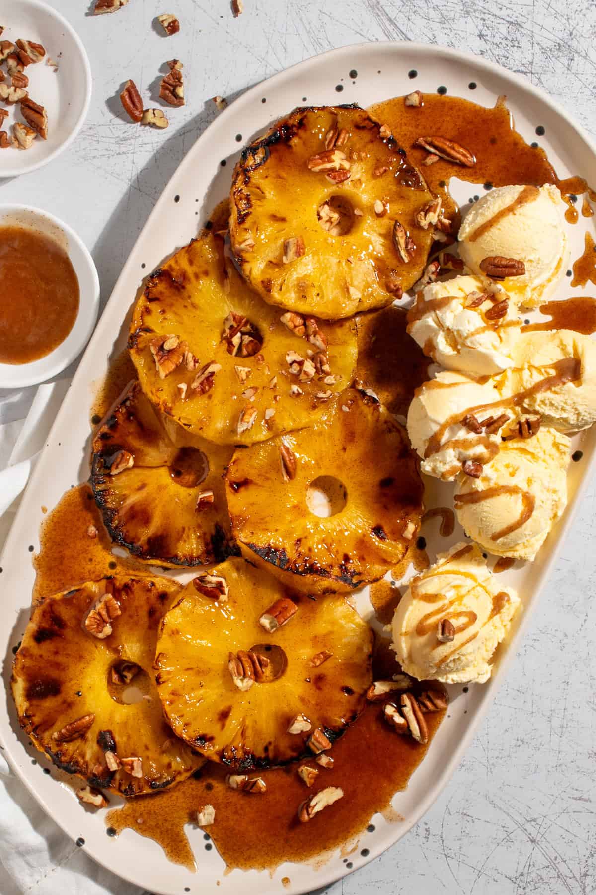 Caramelised Roasted Pineapple with Cinnamon Butter on a large white oval plate with scoops of ice cream on the side.