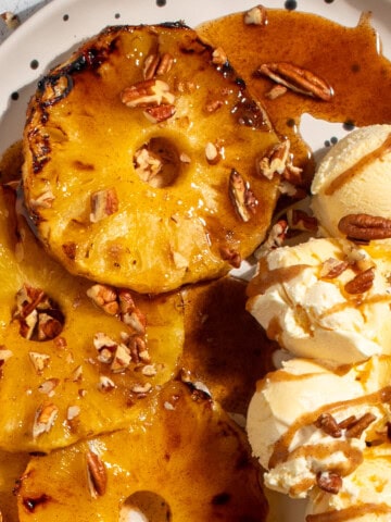 Caramelised Roasted Pineapple with Cinnamon Butter on a large white oval plate with scoops of ice cream on the side.