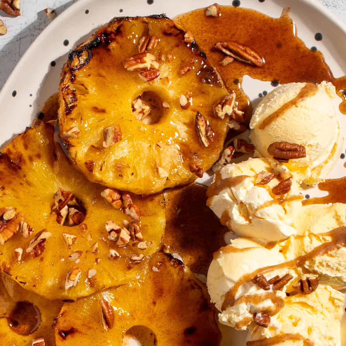 Caramelised Roasted Pineapple with Cinnamon Butter on a large white oval plate with scoops of ice cream on the side.