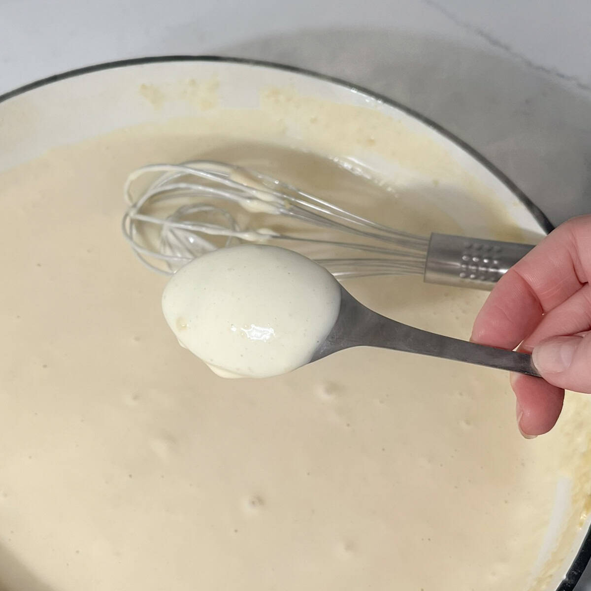 White sauce coating the back of a tablespoon to show the consistency.