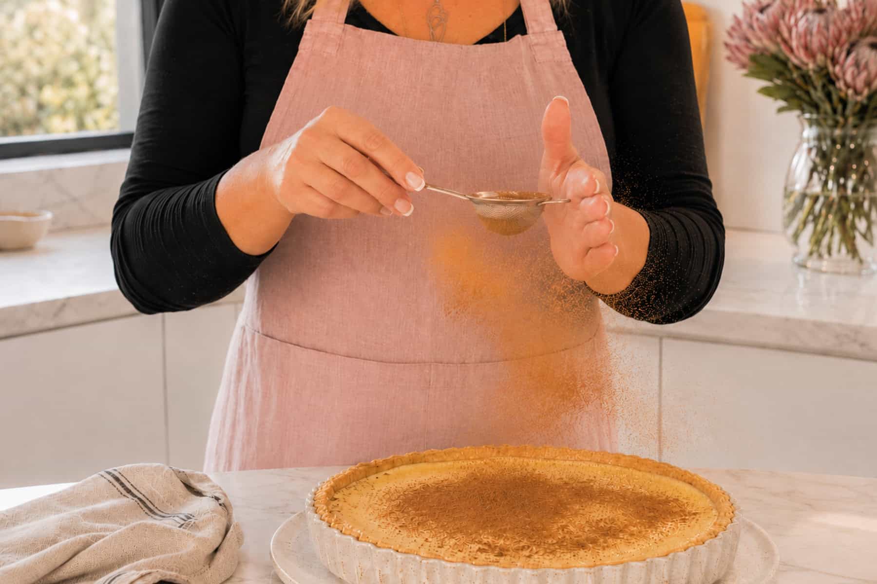 Maretha dusting a milk tart with cinnamon.