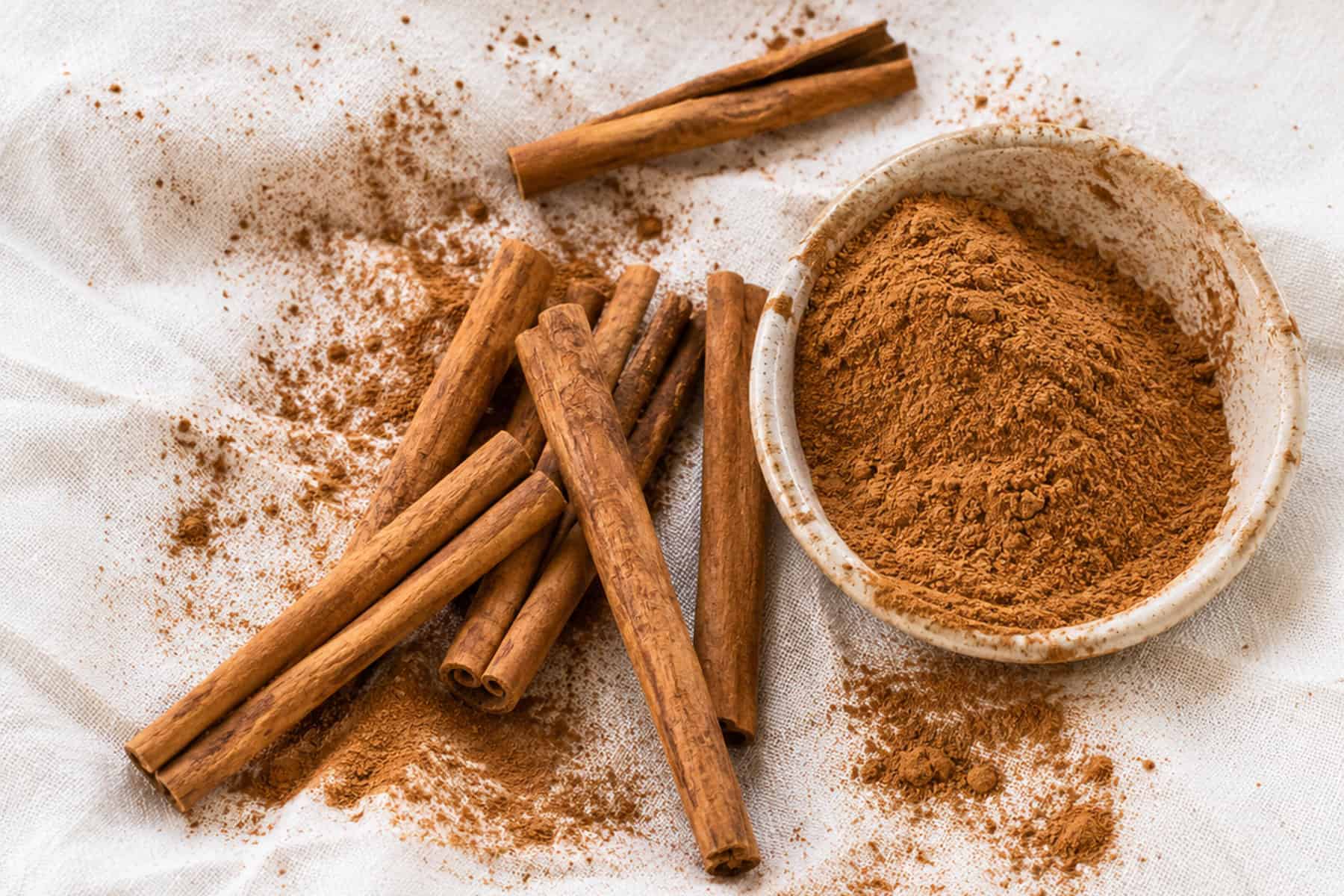 Cinnamon sticks and ground cinnamon on a white linen table cloth.